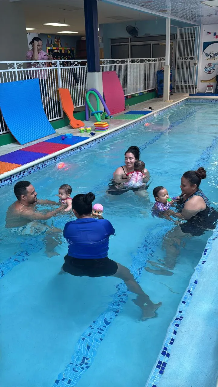Bebés en la piscina acompañados por sus padres y una instructora durante una clase